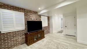 Unfurnished living room with brick wall, light wood finished floors, and recessed lighting