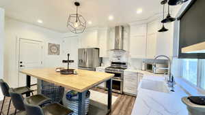 Kitchen featuring tasteful backsplash, light stone countertops, wall chimney exhaust hood, stainless steel appliances, and white cabinetry