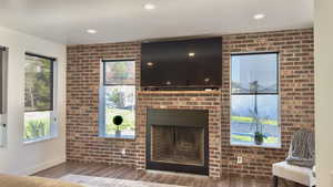 Living room featuring brick wall, a fireplace, wood finished floors, and recessed lighting