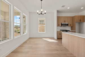 Kitchen featuring tasteful backsplash, appliances with stainless steel finishes, a chandelier, pendant lighting, and light wood-style flooring