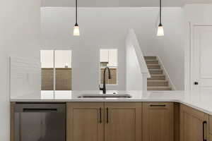 Kitchen featuring stainless steel dishwasher, brown cabinetry, light stone counters, and decorative light fixtures