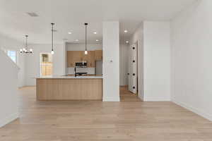 Kitchen with hanging light fixtures, decorative backsplash, recessed lighting, light wood-type flooring, and stainless steel microwave