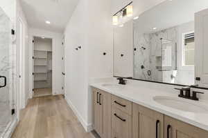 Full bathroom featuring a marble finish shower, a walk in closet, double vanity, and light wood-type flooring