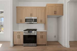 Kitchen featuring stainless steel appliances, tasteful backsplash, light wood-style floors, light brown cabinets, and light stone countertops
