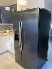 Kitchen featuring stainless steel refrigerator with ice dispenser, white cabinets, decorative backsplash, light tile patterned floors, and light stone countertops