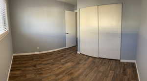 Unfurnished bedroom featuring a closet and dark wood-style floors