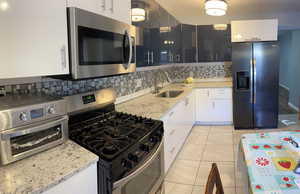Kitchen with appliances with stainless steel finishes, tasteful backsplash, light stone counters, light tile patterned floors, and white cabinetry