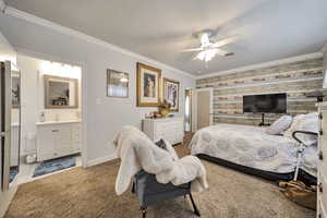 Bedroom featuring ornamental molding, light colored carpet, an accent wall, ceiling fan, and ensuite bath