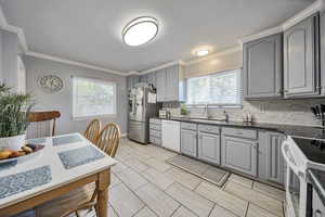 Kitchen featuring gray cabinetry, white appliances, ornamental molding, tasteful backsplash, and dark stone countertops