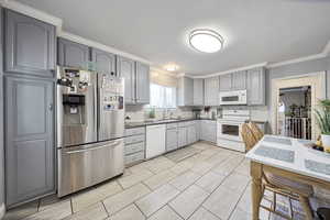 Kitchen featuring gray cabinetry, crown molding, white appliances, and tasteful backsplash