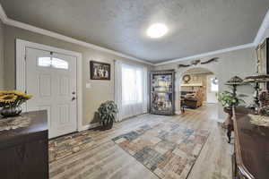 Foyer with ornamental molding, arched walkways, light wood-style floors, a textured ceiling, and a textured wall