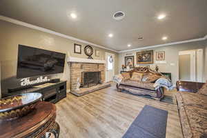 Living room featuring ornamental molding, recessed lighting, wood finished floors, and a stone fireplace