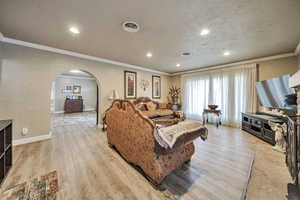 Living room with ornamental molding, arched walkways, a textured ceiling, light wood-style flooring, and recessed lighting