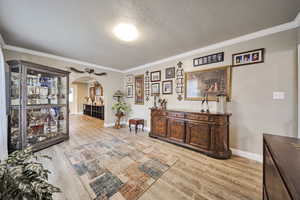 Interior space with arched walkways, a textured ceiling, light wood finished floors, and ornamental molding