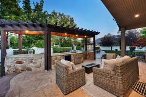 Patio terrace at dusk with a patio area, exterior kitchen, a pergola, and an outdoor living space with a fire pit