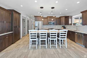 Kitchen featuring dark brown cabinetry, backsplash, a kitchen bar, light stone counters, and a kitchen island