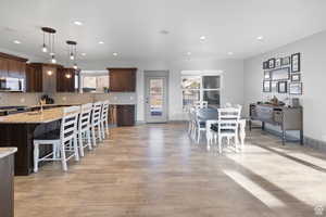 Kitchen featuring dark brown cabinetry, hanging light fixtures, a kitchen breakfast bar, light stone counters, and backsplash