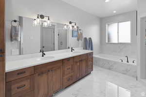 Bathroom featuring double vanity, a bath, light marble finish floors, and recessed lighting