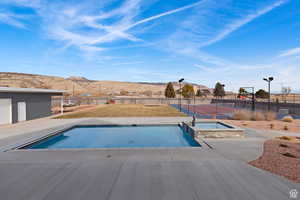 View of pool with a pool with connected hot tub, a mountain view, a patio, and a tennis court