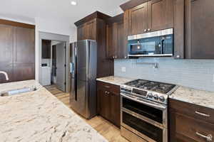 Kitchen featuring appliances with stainless steel finishes, light stone counters, dark brown cabinets, and recessed lighting