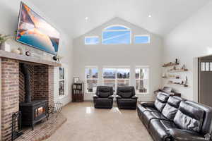 Living area with a wood stove, light carpet, and high vaulted ceiling