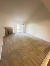Unfurnished living room with a fireplace, vaulted ceiling, and carpet floors