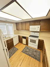 Kitchen featuring light countertops, white appliances, light wood-type flooring, and brown cabinetry