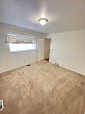 Carpeted spare room featuring a textured ceiling and baseboards