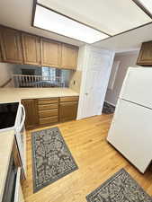 Kitchen featuring white appliances, light countertops, brown cabinets, and light wood-style flooring