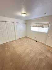 Unfurnished bedroom with two closets, carpet floors, and a textured ceiling