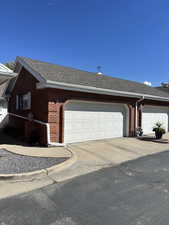 View of side of property with a shingled roof, brick siding, driveway, and a garage