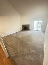 Unfurnished living room featuring a brick fireplace, lofted ceiling, and carpet