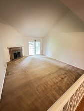 Unfurnished living room featuring a fireplace, carpet flooring, and vaulted ceiling