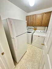 Laundry room featuring separate washer and dryer, a textured ceiling, cabinet space, and light floors