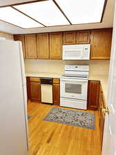 Kitchen with white appliances, light countertops, brown cabinets, and light wood-style flooring