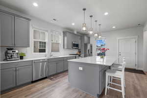 Kitchen with gray cabinets, appliances with stainless steel finishes, light wood-style flooring, backsplash, and recessed lighting