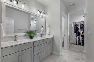 Bathroom with a stall shower, double vanity, a walk in closet, and light marble finish floors
