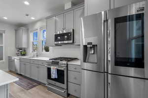 Kitchen with appliances with stainless steel finishes, gray cabinets, backsplash, recessed lighting, and light wood-style flooring
