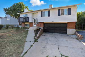 Bi-level home featuring driveway, brick siding, a chimney, and a garage