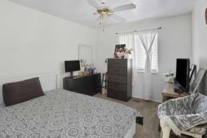 Bedroom with light carpet, ceiling fan, and a desk