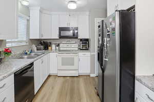 Kitchen with appliances with stainless steel finishes, white cabinetry, light countertops, and light wood-style floors
