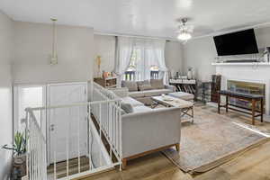 Living area with wood finished floors, a fireplace, a ceiling fan, and a textured ceiling