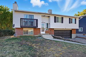 Split foyer home featuring brick siding, a chimney, and an attached garage