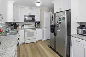 Kitchen with stainless steel appliances, white cabinets, light countertops, and light wood-type flooring
