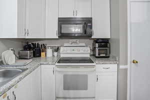 Kitchen featuring electric range, black microwave, white cabinets, and light countertops