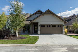 Craftsman-style home with a garage, concrete driveway, stone siding, a front lawn, and a mountain view