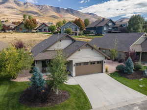 Craftsman-style house featuring a mountain view, a front lawn, an attached garage, concrete driveway, and stone siding