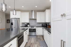 Kitchen with appliances with stainless steel finishes, decorative backsplash, wall chimney exhaust hood, recessed lighting, and white cabinets