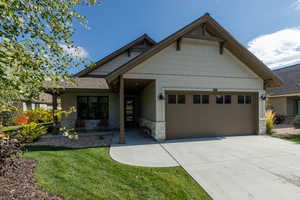 Craftsman house featuring stone siding, roof with shingles, concrete driveway, a front yard, and an attached garage