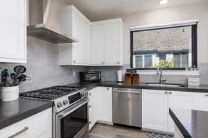 Kitchen with appliances with stainless steel finishes, wall chimney exhaust hood, white cabinetry, decorative backsplash, and recessed lighting